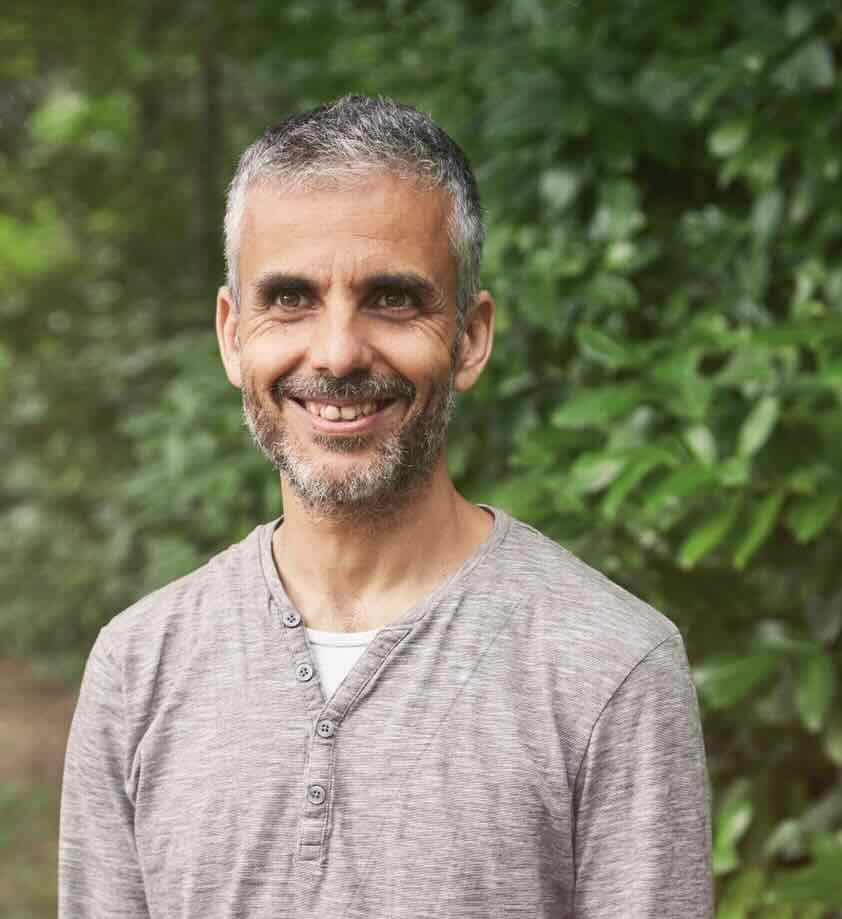 Homem de meia-idade com barba cinzenta sorri perante vegetação